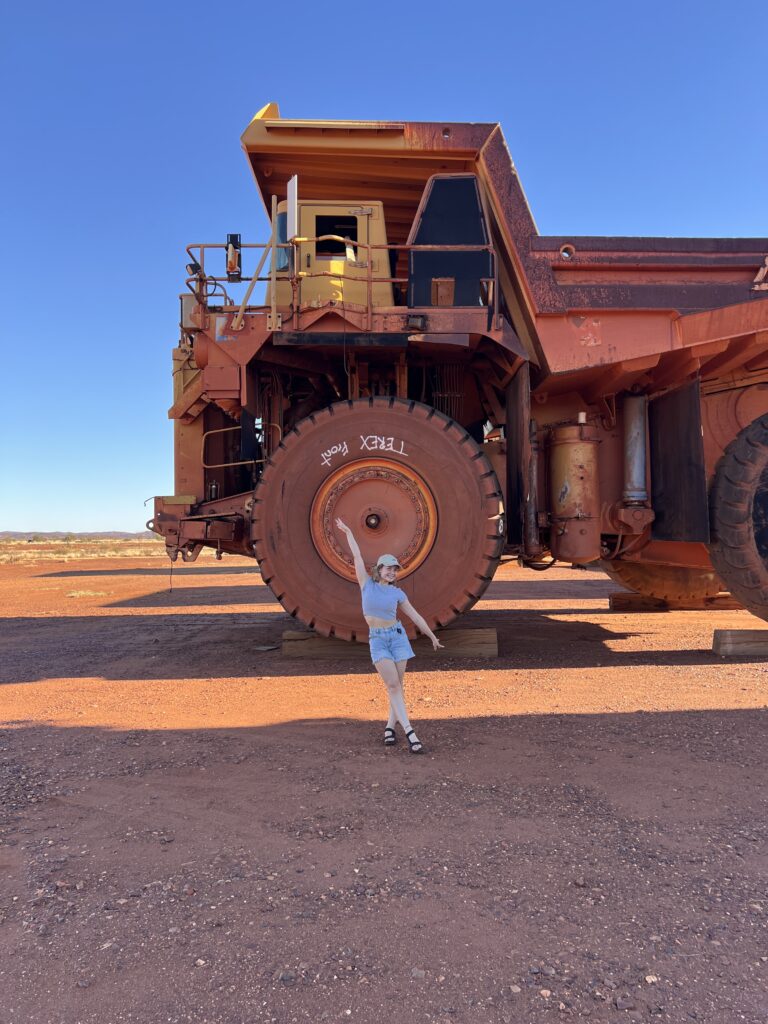 young woman stands in front of large mining truck in outback Australia